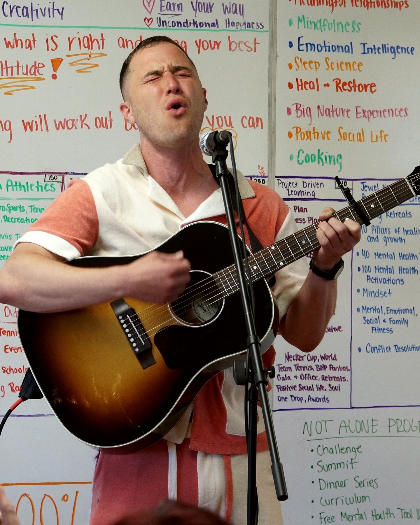 Mike Posner singing with an acoustic guitar in front of the foundation's whiteboards