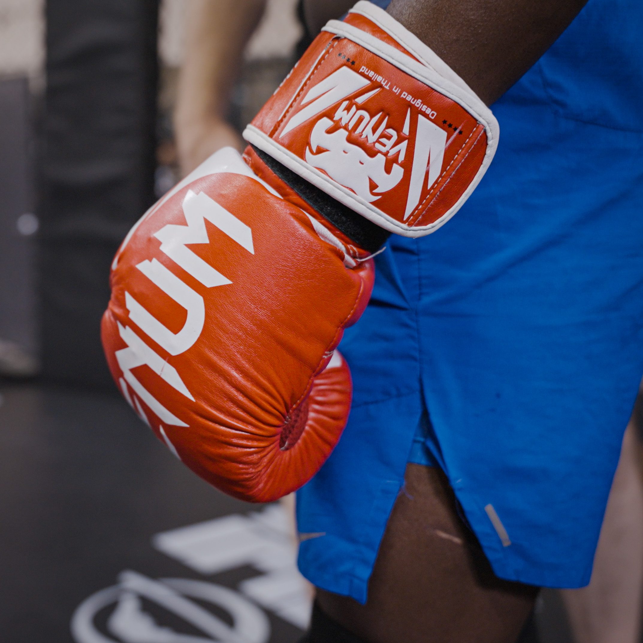Manel Kape's orange Venum glove against blue fight shorts